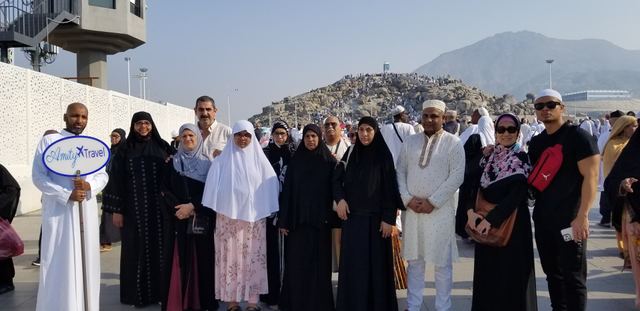 Amity Umrah group with the Amity Travel sign at Arafat, Jabal al-Rahmah behind