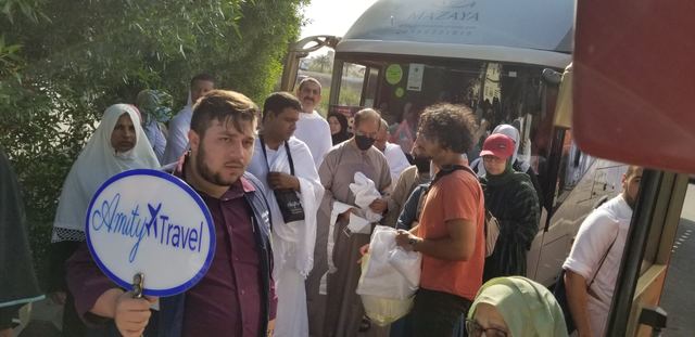 Amity staff holding the Amity Travel sign as travelers board the group bus