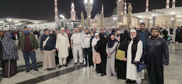 Amity Umrah group at night in the courtyard of Masjid an-Nabawi, the green dome and umbrellas behind