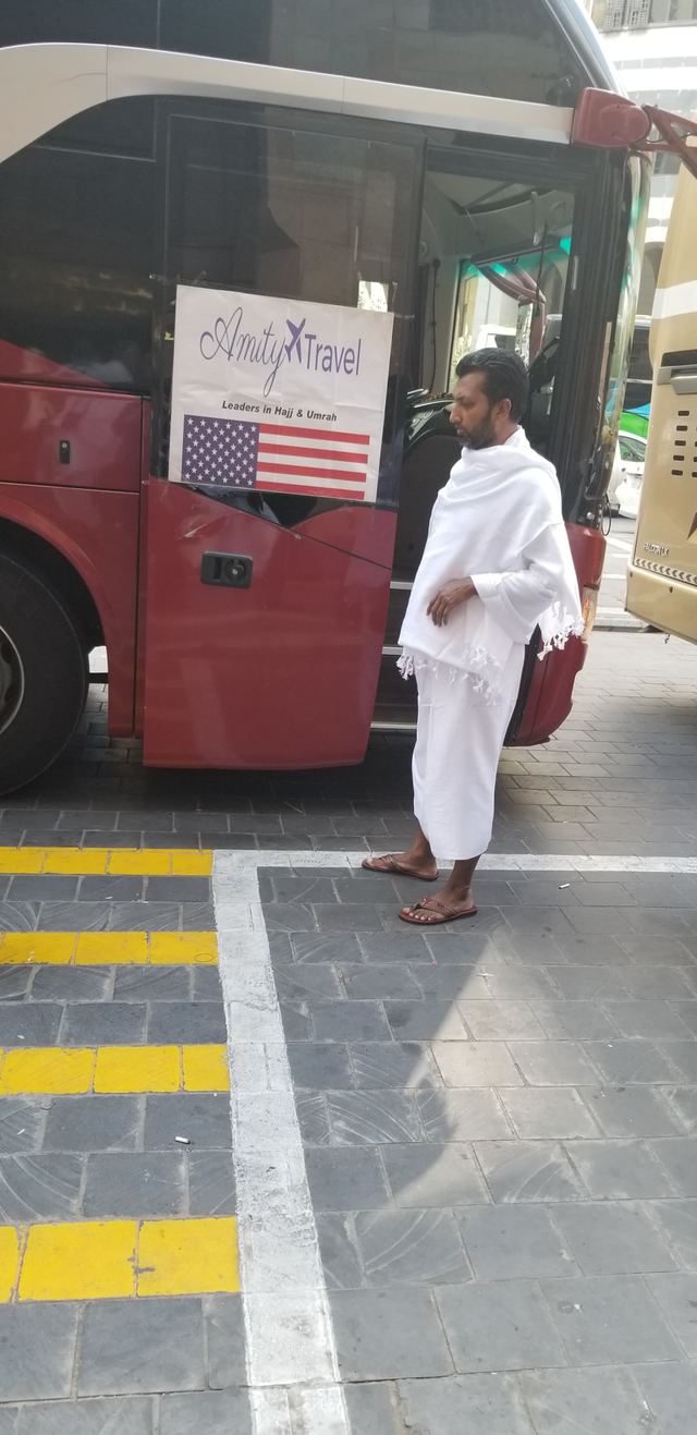 An Amity traveler in ihram beside the Amity group bus with its Amity Travel sign