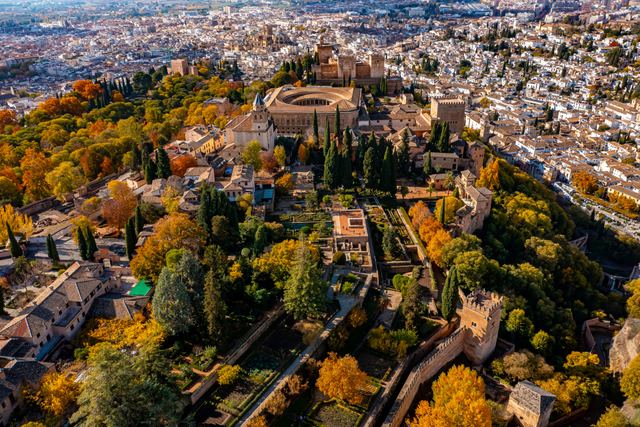 Aerial view of the Alhambra in Granada among autumn trees, with the city spreading behind.