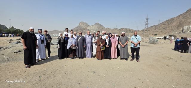 Amity Umrah group lined up on open ground with jagged mountains behind