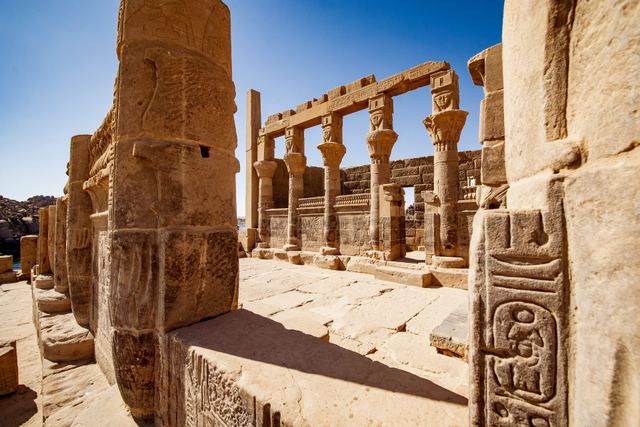 Carved stone columns and walls covered in hieroglyphs at Philae Temple under a clear blue sky.