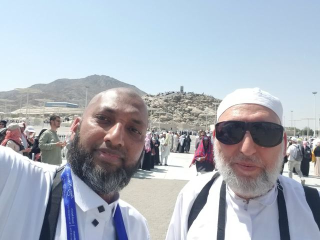 Amity group leader taking a selfie with a traveler at Arafat, Jabal al-Rahmah behind
