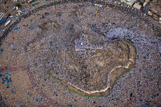 Aerial view of pilgrims in white filling the plain around the rocky hill of Jabal al-Rahmah at Arafat.