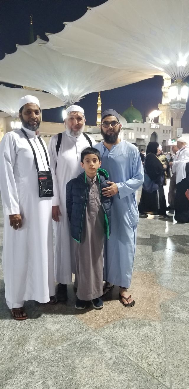 Amity travelers and a boy at night in the courtyard of Masjid an-Nabawi, the green dome behind