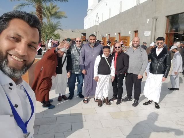 Amity group leader taking a selfie with travelers beside a white wall and palm trees